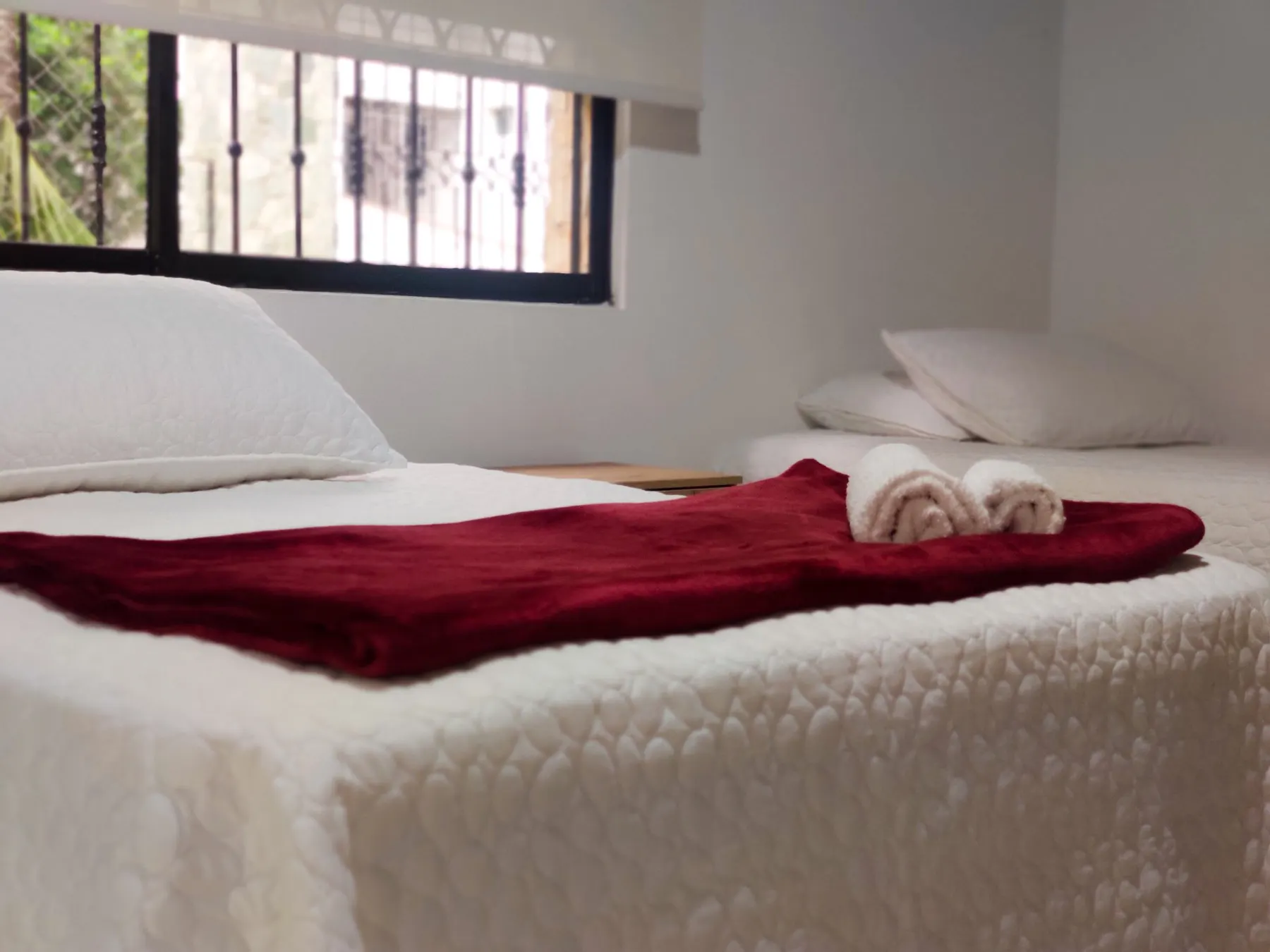 Chambre privée de la maison de convalescence avec literie blanche, un jeté rouge et des serviettes pliées