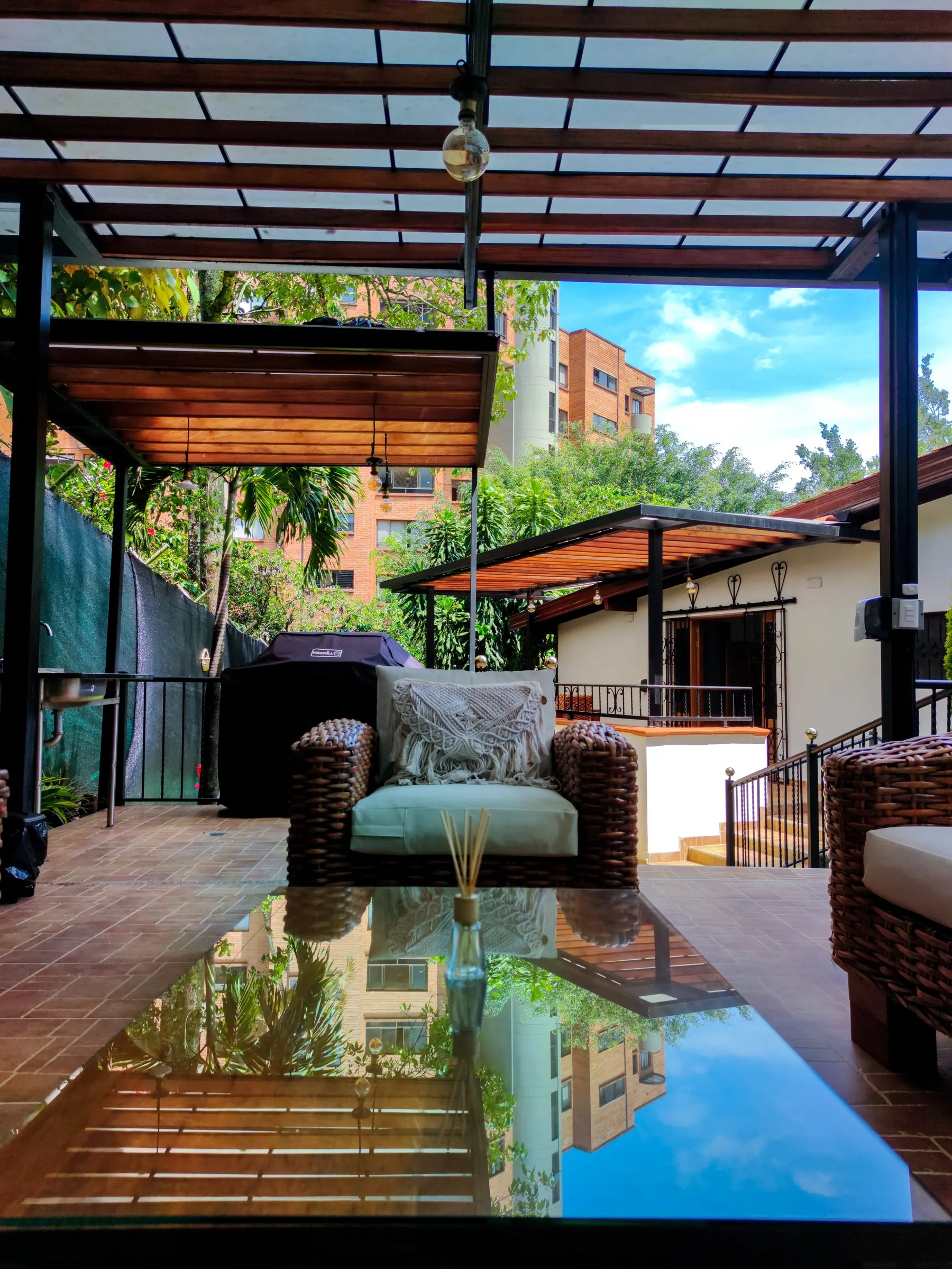 Terrasse couverte avec un canapé et une table en verre entourés de plantes