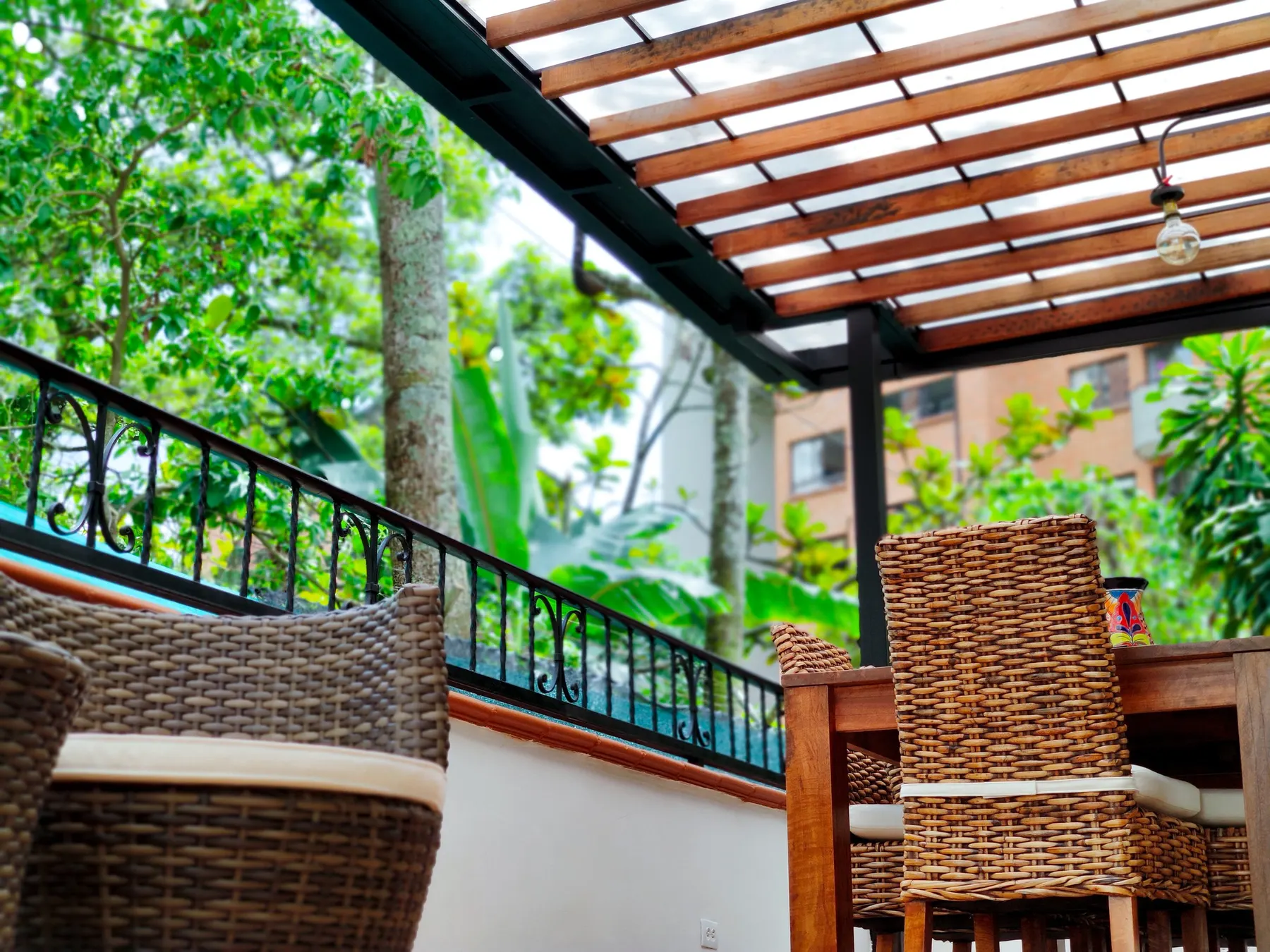 Terrasse couverte avec une table en bois, des chaises en osier et une vue sur les arbres