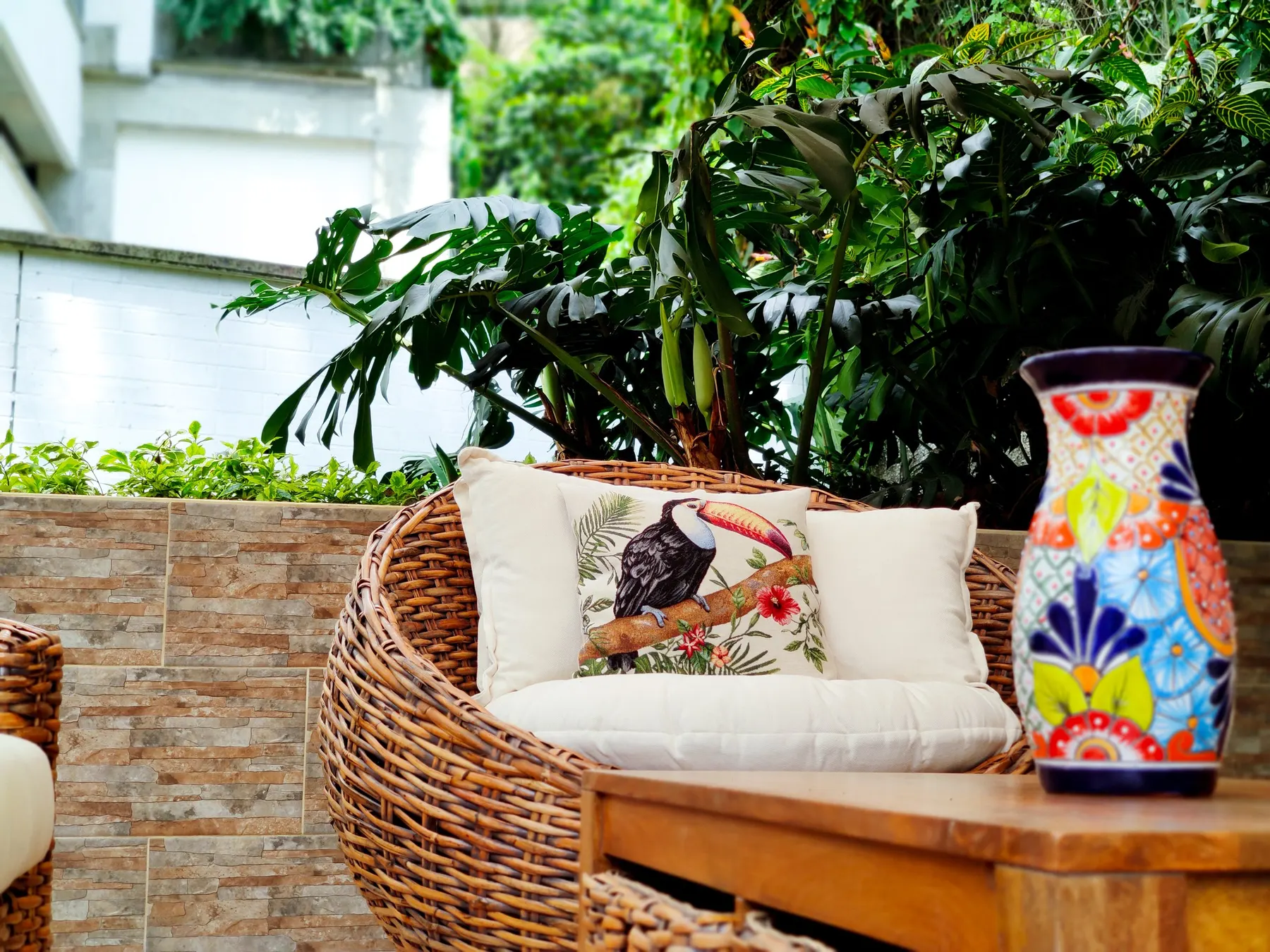 Coin salon de la terrasse avec un siège en osier, des coussins et un vase peint